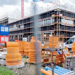 emmendingen-gebaeude-baustelle-2021.jpg Baustellenansicht des Sutter-Neubaus in Emmendingen mit eingerüstetem Gebäude, bunten Baucontainern und gelagertem Baumaterial im Vordergrund.