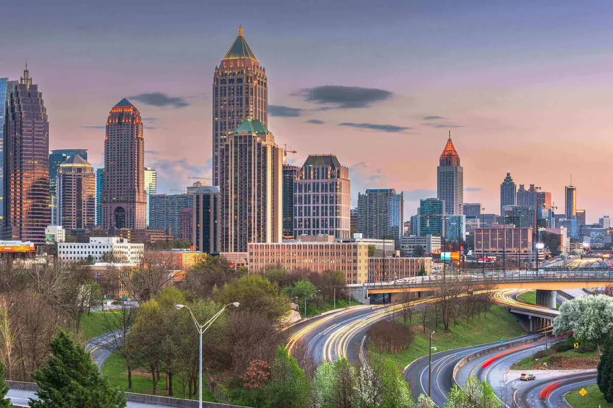 Skyline von Atlanta, USA, bei Sonnenuntergang mit beleuchteten Hochhäusern und fließendem Abendverkehr auf den geschwungenen Highways im Vordergrund.