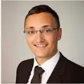Heiser mit Brille, Hemd und Krawatte vor hellem, neutralem Hintergrund.