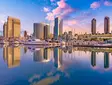 Panoramic view of San Diego skyline at sunset with high-rise buildings, yachts in the marina, and colorful sky.