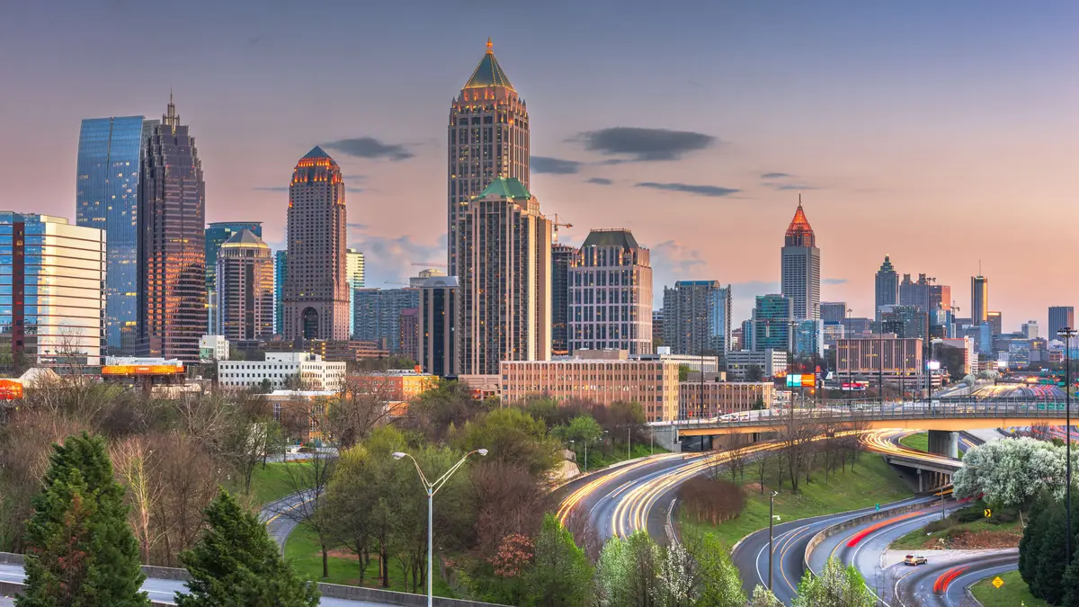 Skyline von Atlanta, USA, bei Sonnenuntergang mit beleuchteten Hochhäusern und fließendem Abendverkehr auf den geschwungenen Highways im Vordergrund.