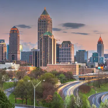 Skyline von Atlanta, USA, bei Sonnenuntergang mit beleuchteten Hochhäusern und fließendem Abendverkehr auf den geschwungenen Highways im Vordergrund.