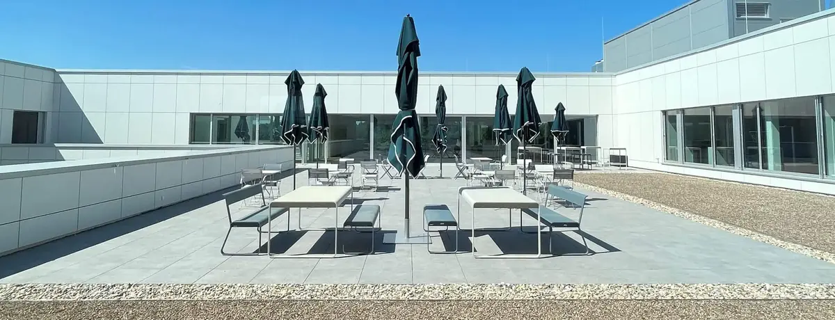 Weitläufige Dachterrasse bei Sutter Medizintechnik mit Tischen, Stühlen und Sonnenschirmen unter blauem Himmel.