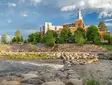 University building beside a river with stone embankment, trees, and a cloudy sky.