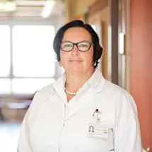 Prof. Schick in weißem Arztkittel und Brille stehend in einem hellen Klinikflur.