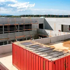 emmendingen-gebaeude-baufortschritt-innenhof-2021.jpg Innenhof des neuen Firmengebäudes der Sutter Medizintechnik GmbH im Rohbauzustand mit eingerüsteter Fassade, einem roten Baucontainer und Blick auf die umliegende Landschaft.