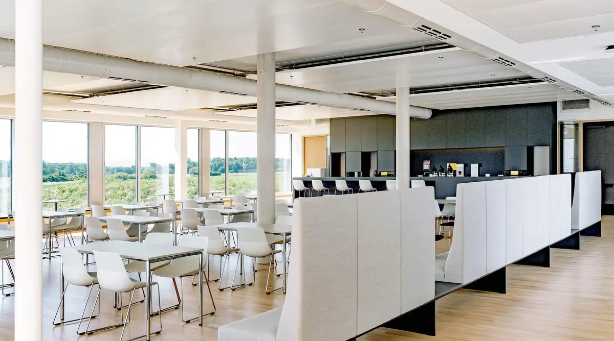 Moderner, lichtdurchfluteter Sozialraum bei Sutter Medizintechnik mit Tischen, Stühlen, einer Bar und großen Fenstern mit Blick ins Grüne.