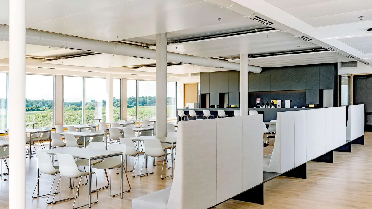 Moderner, lichtdurchfluteter Sozialraum bei Sutter Medizintechnik mit Tischen, Stühlen, einer Bar und großen Fenstern mit Blick ins Grüne.