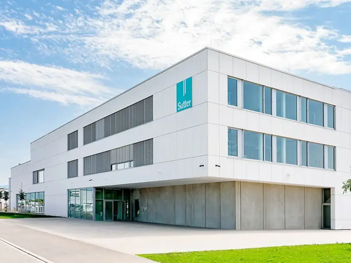 sutter-medizintechnik-unternehmenssitz-emmendingen.jpg Moderner Unternehmenssitz von Sutter Medizintechnik in Emmendingen mit weißer Fassade, großen Glasflächen und Sutter-Logo.