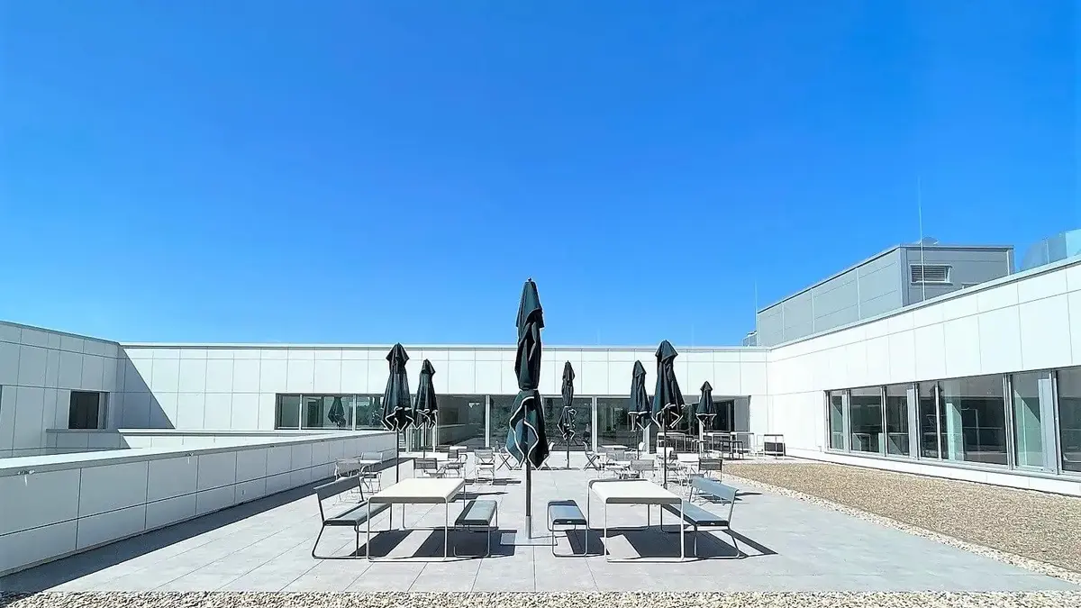 Weitläufige Dachterrasse bei Sutter Medizintechnik mit Tischen, Stühlen und Sonnenschirmen unter blauem Himmel.