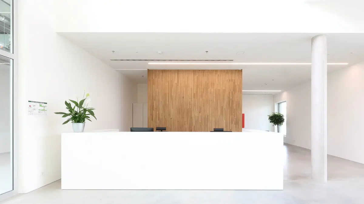 Moderner Empfangsbereich mit weißem Tresen, Holzverkleidung im Hintergrund und großen Pflanzen – Standort Sutter Medizintechnik.